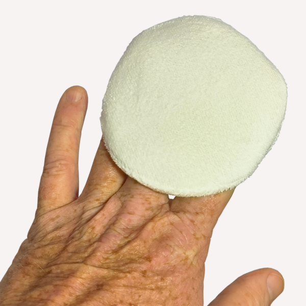 Hand holding white microfibre applicator pad.