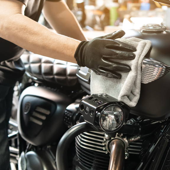 Man performing winter motorcycling cleaning on black motorcycle using white microfiber cloth with black glove. 