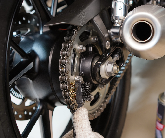 Close-up of a person cleaning motorcycle exterior parts with microfibre cloth.