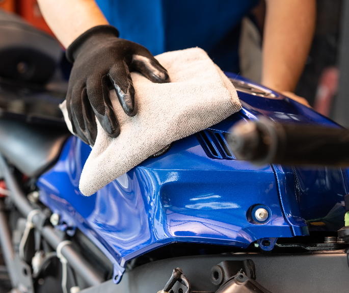 Close-up of a person cleaning a motorcycle chain using a brush.