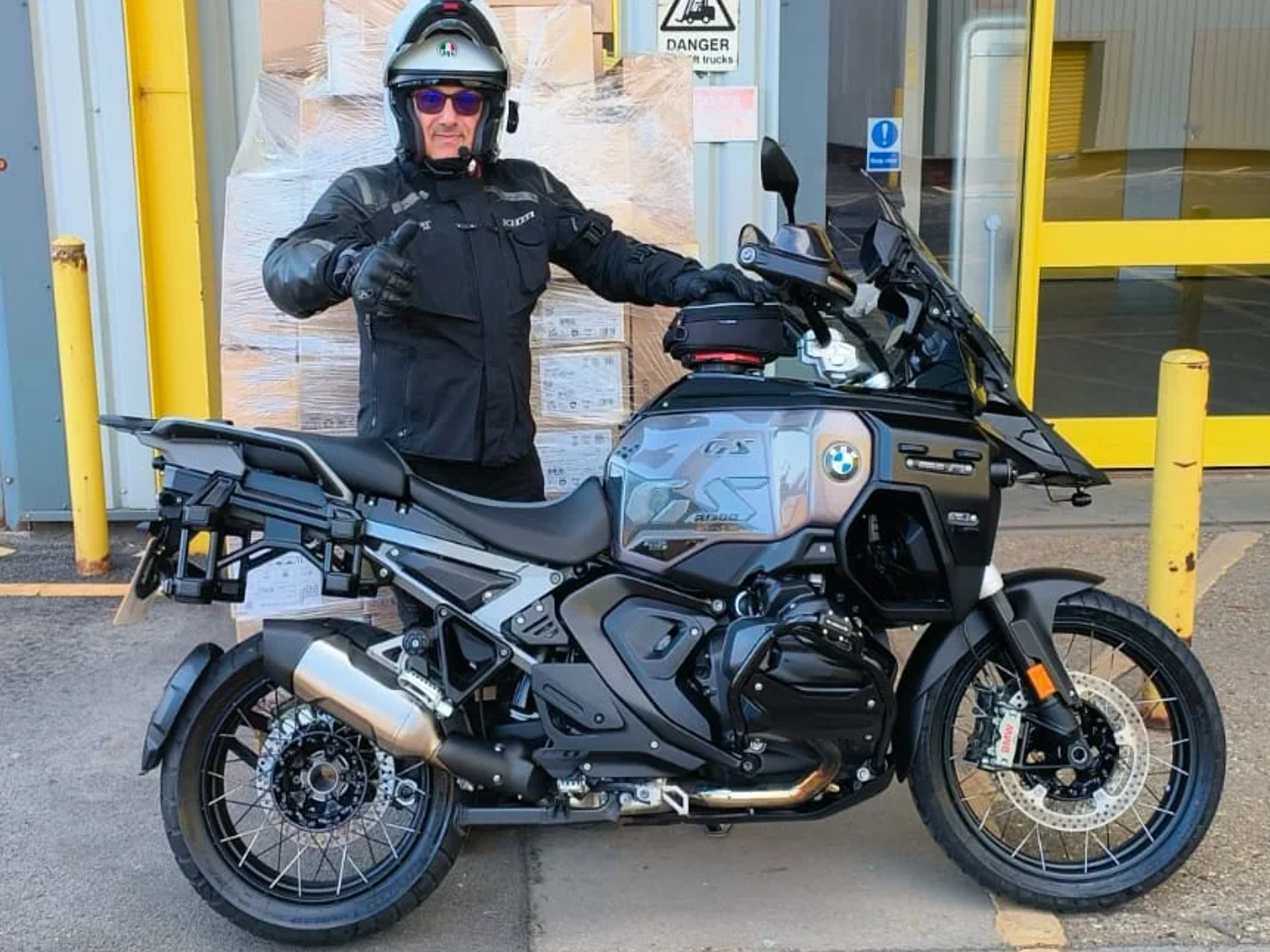 Man stood in biker attire with thumb up stood next to his BMW bike.