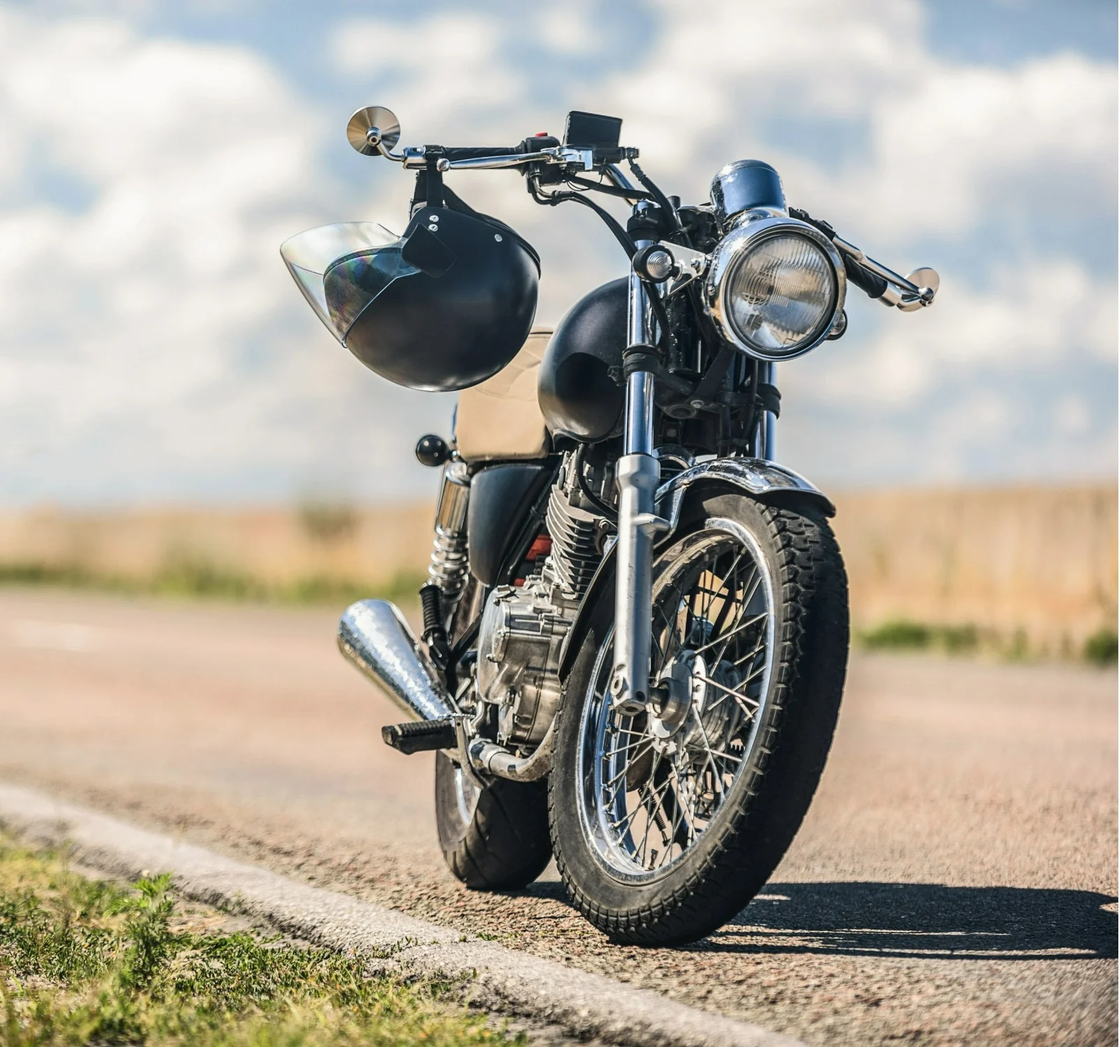 A motorbike parked on the side of a country road with cloudy skies in the background.