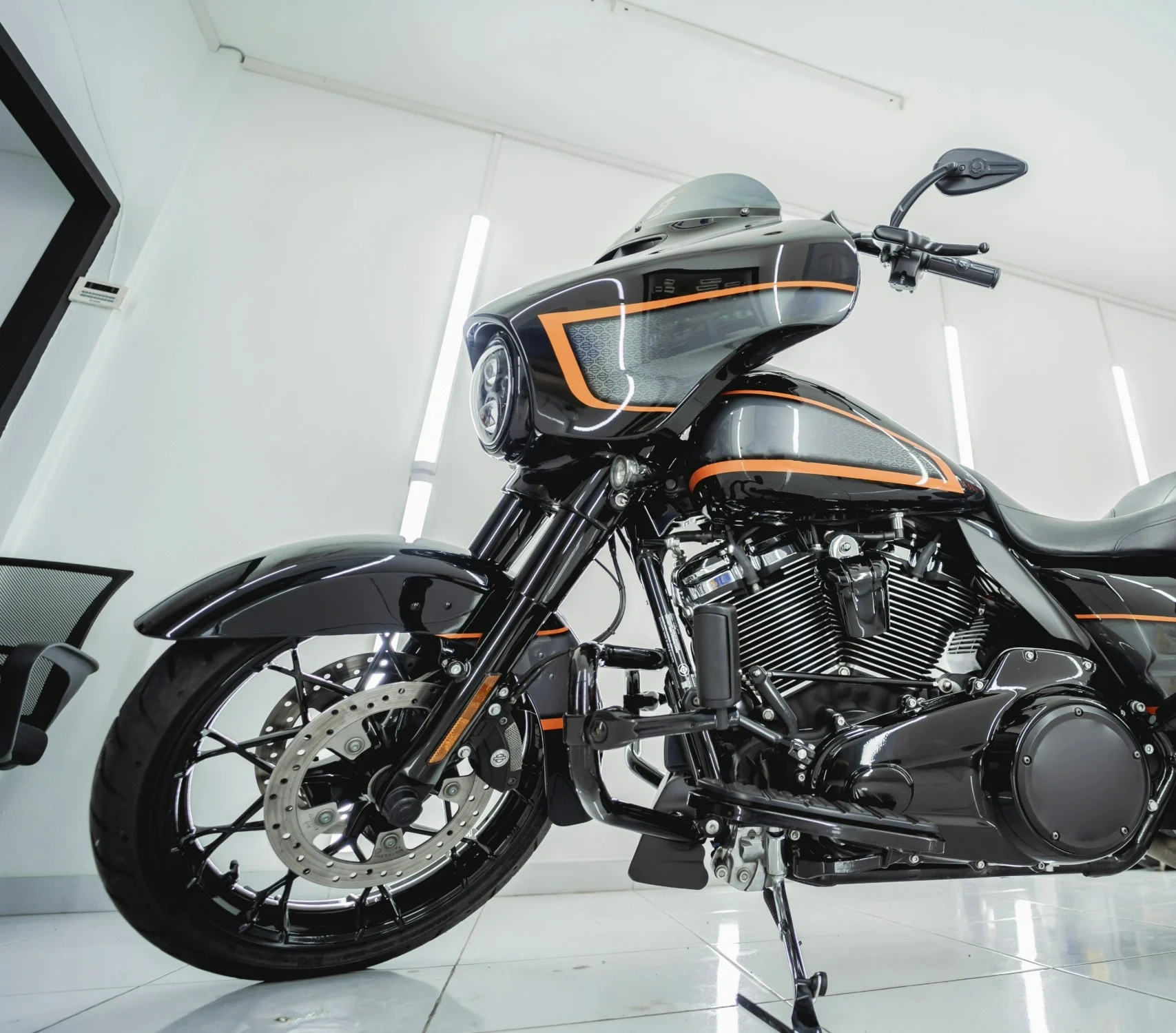 A black and orange motorbike propped up in a bright room.