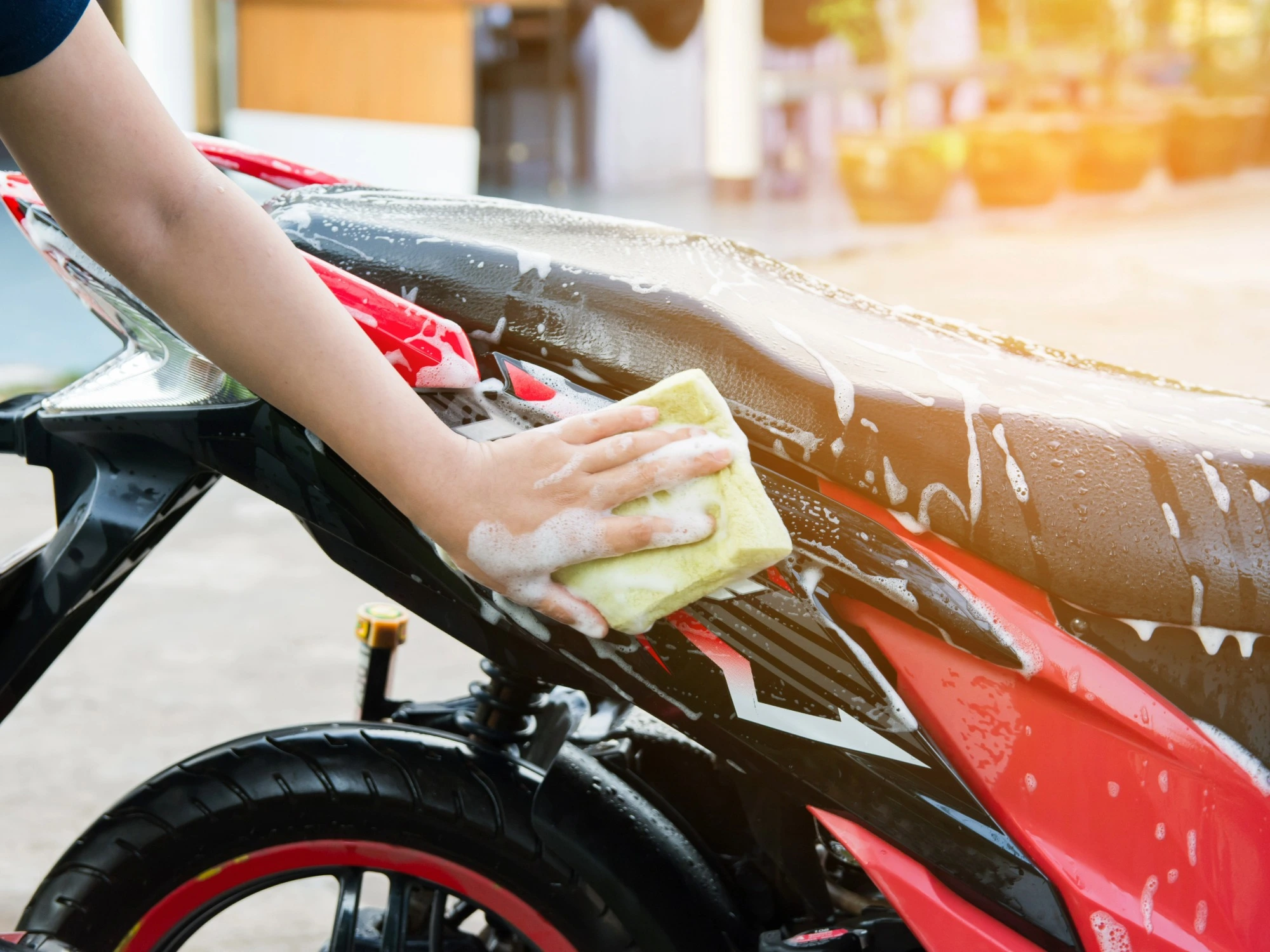 The back of a red motorbike being cleaned with a yellow sponge